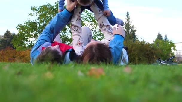 Šťastná rodina ležet na trávníku. Matka a otec drží svého syna v náručí nad hlavou, dětské úsměvy. Na pozadí slunce a obloha šťastné tváře rodiče a dítě. — Stock video
