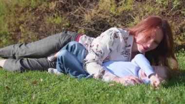 Mutlu bir aile çimenlerin üstünde dinlenme. Şefkat ve sevgi ile anne çocuğunu evlat güler sarılmak. Mutlu çocukluk