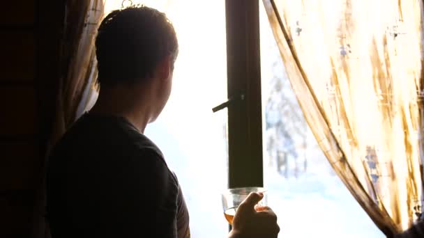 Día helado de invierno. El tipo temprano en la mañana de pie en la ventana y beber té caliente . — Vídeos de Stock