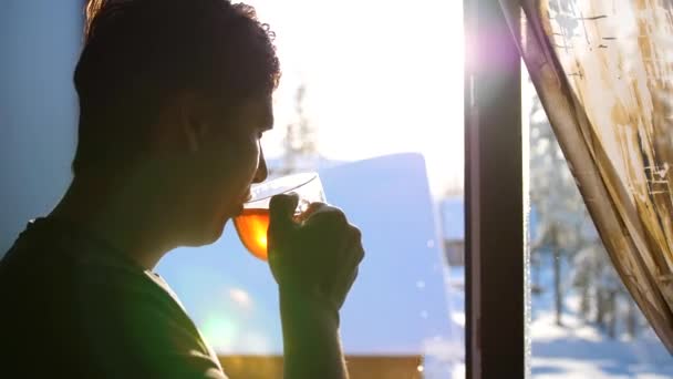 Día helado de invierno. El tipo temprano en la mañana de pie en la ventana y beber té caliente . — Vídeos de Stock