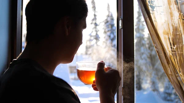 Зимний морозный день. Парень рано утром стоял у окна и пил горячий чай. . — стоковое фото