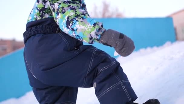 一个小孩在冬天的公园里散步。玩耍和微笑的婴儿爬上山, 再次坠落上升。积极的休息和游戏. — 图库视频影像