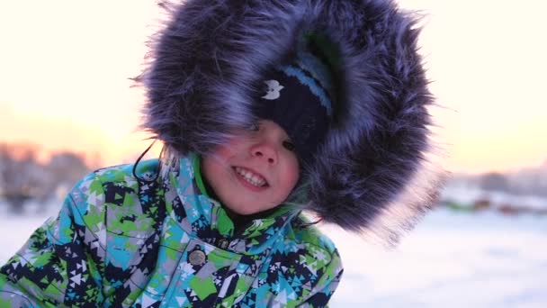 Un niño pequeño camina en el parque de invierno. Jugando y sonriendo bebé en la blanca nieve esponjosa. Cara de cerca. Descanso activo y juegos . — Vídeo de stock