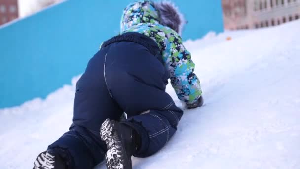 一个小孩在冬天的公园里散步。玩耍和微笑的婴儿爬上山, 再次坠落上升。积极的休息和游戏. — 图库视频影像
