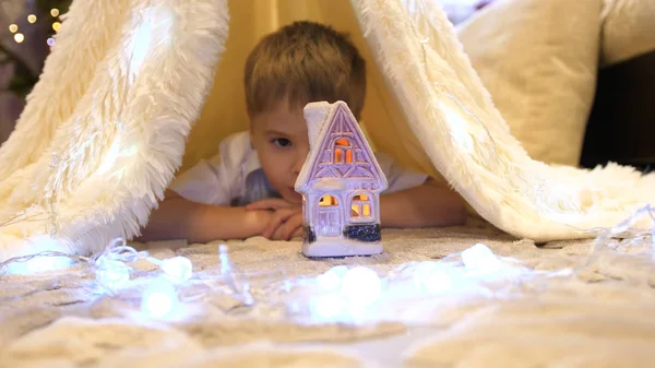 L'enfant joue dans la chambre d'enfant dans une tente avec une lumière de Noël. Bonne enfance Images De Stock Libres De Droits