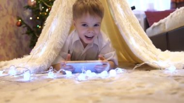 Smartphone bir çadırda Noel ışık ile çocuk odasında oynayan çocuk. Mutlu çocukluk