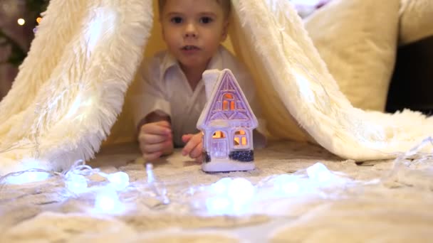 El niño juega en la habitación de los niños en una tienda de campaña con una luz de Navidad. Feliz infancia. — Vídeos de Stock