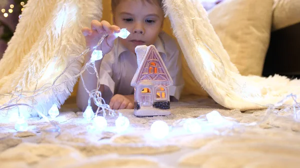Copilul se joacă în camera copiilor într-un cort cu o lumină de Crăciun. Copilărie fericită Fotografie de stoc