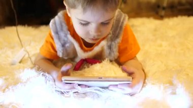 Çocuk yumuşak beyaz battaniye çocuk odasında yatıyor. Smartphone çizgi film izliyor. Noel çelenk. Mutlu çocukluk