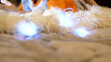 Mutlu çocukluk. Çocuk yumuşak beyaz battaniye çocuk odasında yatıyor. Smartphone çizgi film izliyor. Noel çelenk.