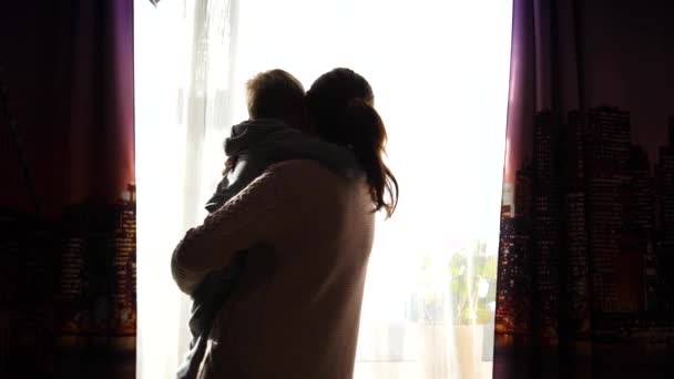 母亲抱着一个小孩子。阳光透过窗户照射。婴孩的笑声和喜悦. — 图库视频影像