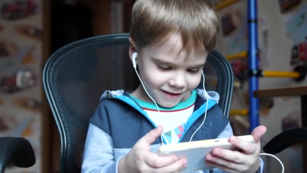 De jongen luistert naar muziek via de hoofdtelefoon. In de kinderkamer het kind geniet van muziek — Stockvideo