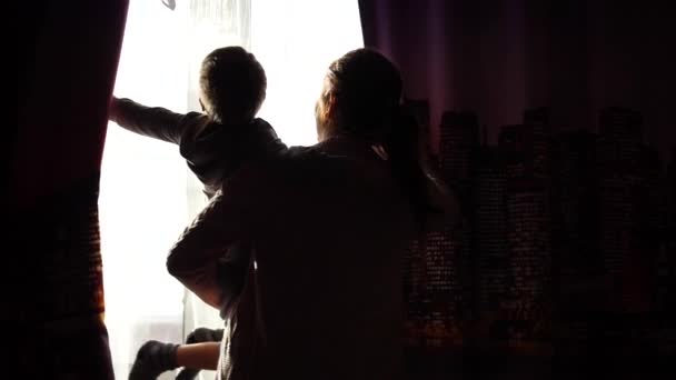 Madre sostiene a un niño por la mañana cerca de la ventana. Temprano en la mañana abren las cortinas, los rayos del sol pasan por la ventana. amanecer — Vídeo de stock