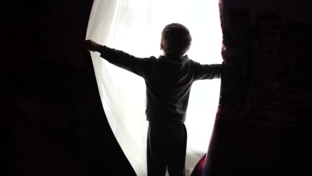 Temprano en la mañana el niño abre las cortinas, los rayos del sol pasan a través de la ventana. amanecer — Vídeo de stock