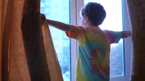 Temprano en la mañana el niño abre las cortinas, los rayos del sol pasan a través de la ventana. amanecer — Vídeos de Stock