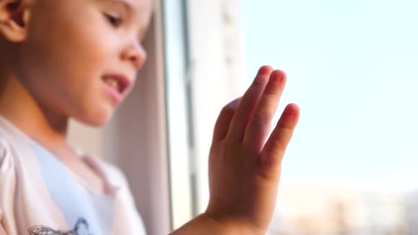 Ein Kind steht neben einem Fenster und beobachtet, wie Schnee auf die Straße fällt. die Nahaufnahme Hand am Glasfenster — Stockvideo
