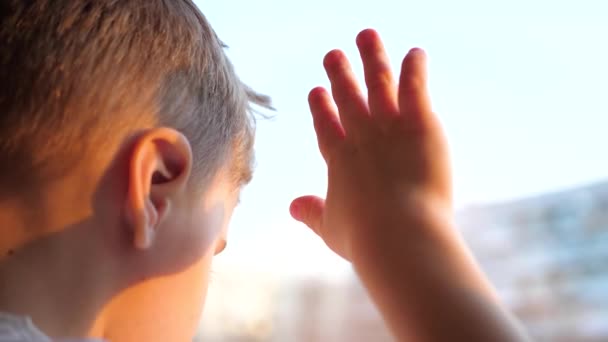 Un bambino sta vicino a una finestra e guarda la neve cadere per strada. La mano di primo piano sulla finestra di vetro — Video Stock