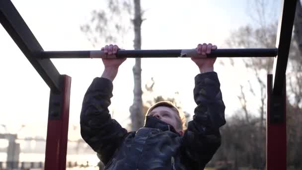 Oefening in de frisse lucht. Jonge sterke man doet oefeningen op de bar. Herfstpark — Stockvideo