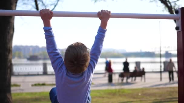 Exercício ao ar livre. Um rapazinho a fazer exercícios no bar. Parque de Verão — Vídeo de Stock