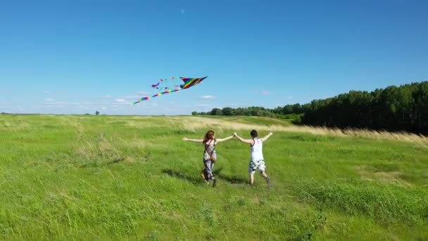 Een jonge man en een meisje dat over het veld loopt. Paar lanceren vliegende vlieger. Familie vakantie. — Stockvideo