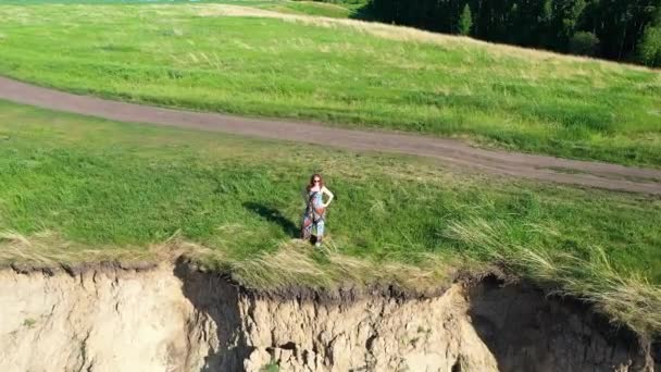 Het meisje staat aan de rand van de klif. Prachtig landschap van berg rivier en bos. Fotograferen vanaf boven — Stockvideo