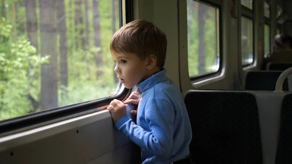 Il ragazzo viaggia in treno e guarda fuori dalla finestra, guardando gli oggetti in movimento fuori dalla finestra. Viaggiare con la famiglia — Foto Stock
