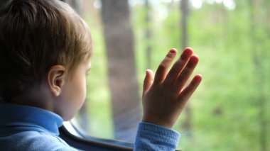 Çocuk trenle seyahat ediyor ve pencereden dışarı bakıyor, pencerenin dışındaki hareketli nesneleri izliyor. El yakın çekim. Aile ile seyahat