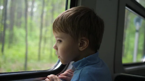 Il ragazzo viaggia in treno e guarda fuori dalla finestra, guardando gli oggetti in movimento fuori dalla finestra. Viaggiare con la famiglia — Foto Stock