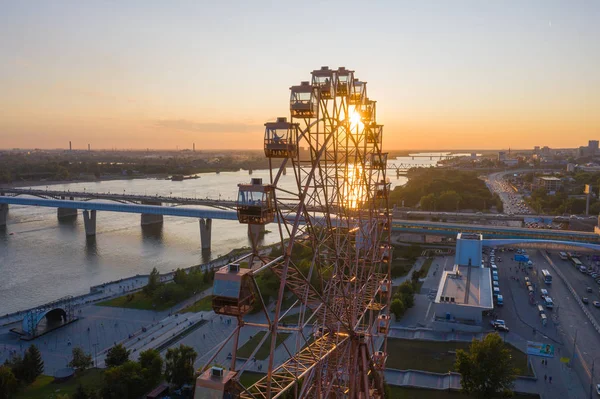 Drone vista roda gigante colorido no parque de diversões na paisagem do rio e da cidade. Parque de diversões com grande roda gigante no fundo verde das terras altas. Vista aérea. Hora do pôr do sol Imagens De Bancos De Imagens