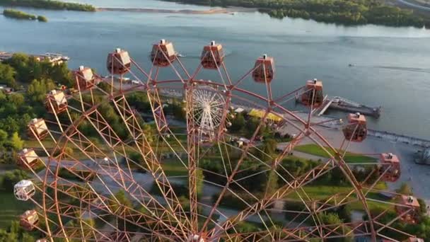 Drone view colorful ferris wheel in amusement park on river and city landscape. Amusement park with large ferris wheel on green highlands background. Aerial view — Stock Video