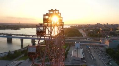 Drone nehir ve şehir manzara üzerinde eğlence parkı renkli dönme dolap görünümü. Yeşil dağlık arka plan üzerinde büyük dönme dolap ile eğlence parkı. Havadan görünüm. Gün batımı zamanı