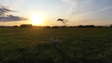 Anne ve çocuk yeşil bir alanda uçurtma ile çalıştırın. Kahkaha ve neşe, şenlikhavası. Sonbahar, Gün Batımı