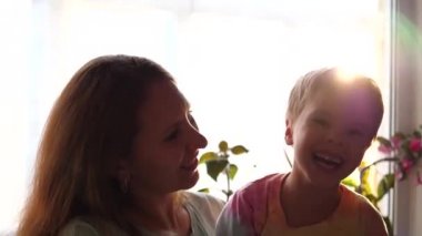 Bir anne oğlunu pencerenin önünde kollarına tutar. Güneş ışınları camdan geçer. İyi bir ruh hali