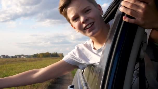 Teen boy looks out the car window and waves. The car is moving on a country road — Stock Video