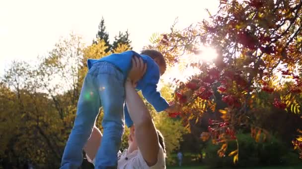 Een jonge vader speelt met een kind, houdt hem in zijn armen, gooit omhoog. De zonnen stralen door het kind. Het lachen en de vreugde van het gezin. — Stockvideo