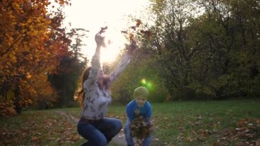 Anne ve çocuk sonbahar parkında sarı yapraklar fırlatıyor. Gülen ve gülümseyen mutlu aile