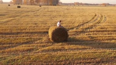 Çocuklar samanlıkta oturuyorlar. Oynayıp gülüyorlar. Kırsal kesimde. Gün batımı