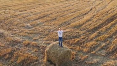 Bir genç samanlıkta duruyor ve ellerini sallıyor. Açık hava eğlencesi. Kırsal kesimde. Gün batımı