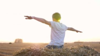 Adam samanlıkta oturuyor. Sahadaki mesafeye bakıyor, uçuşu taklit ediyor. Kırsal kesimde. Gün batımı