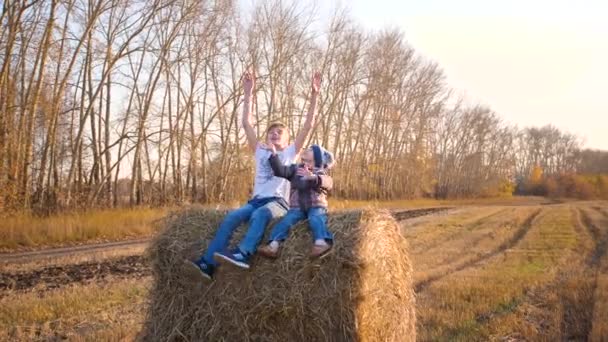 Děti sedí na kupce sena. Hrajou a smějou se. Venkov. Západ slunce — Stock video