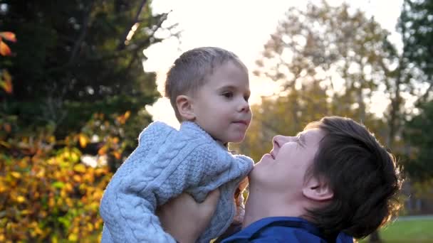 A young father plays with a child, holding him in his arms, throws up. The suns rays through the child. The laughter and joy of the family. — Stock Video