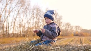 Bir çocuk samanlıkta oturuyor. Oynuyor ve gülüyor. Gün batımı