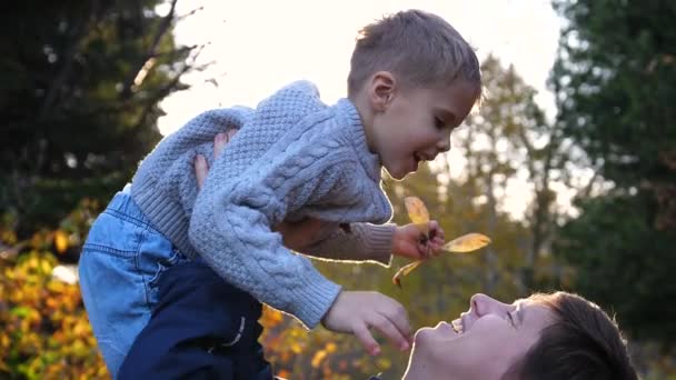 Mladý otec hraje s dítětem, drží ho v náručí a hází. Sluneční paprsky dopadají na dítě. Smích a radost rodiny. — Stock video