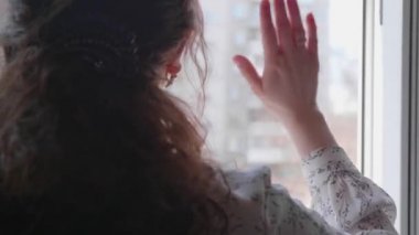 Koruyucu maskeli kız hastanedeymiş. Kız açık bir pencereden iletişim kuruyor, selamlar ve öpücükler gönderiyor. Sağlık ve can güvenliğinin önlenmesi ve korunması.