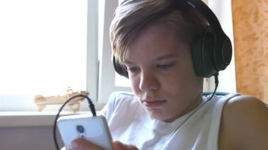 Genç bir insan kulaklık ve telefon kullanarak müzik dinler. Adam pencerenin yanındaki odada.