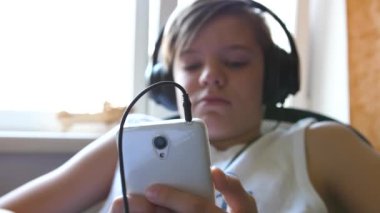 Genç bir insan kulaklık ve telefon kullanarak müzik dinler. Adam pencerenin yanındaki odada.