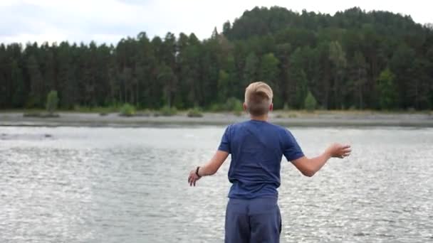 Adolescente joga na margem do rio. Ele atira pedras para a água — Vídeo de Stock