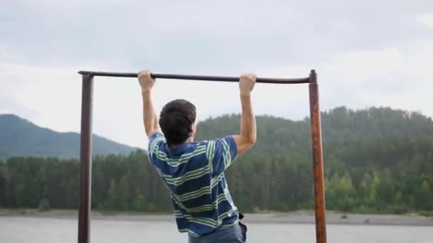Exercise in the fresh air. Young strong guy doing exercises on the bar. Autumn park — Stock Video