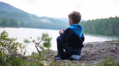 Bir çocuk nehir kıyısında bir uçurumda oturuyor. Akşam vakti.
