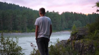 Bir genç uçurumun kıyısında duruyor. Dağlara bakıyor.